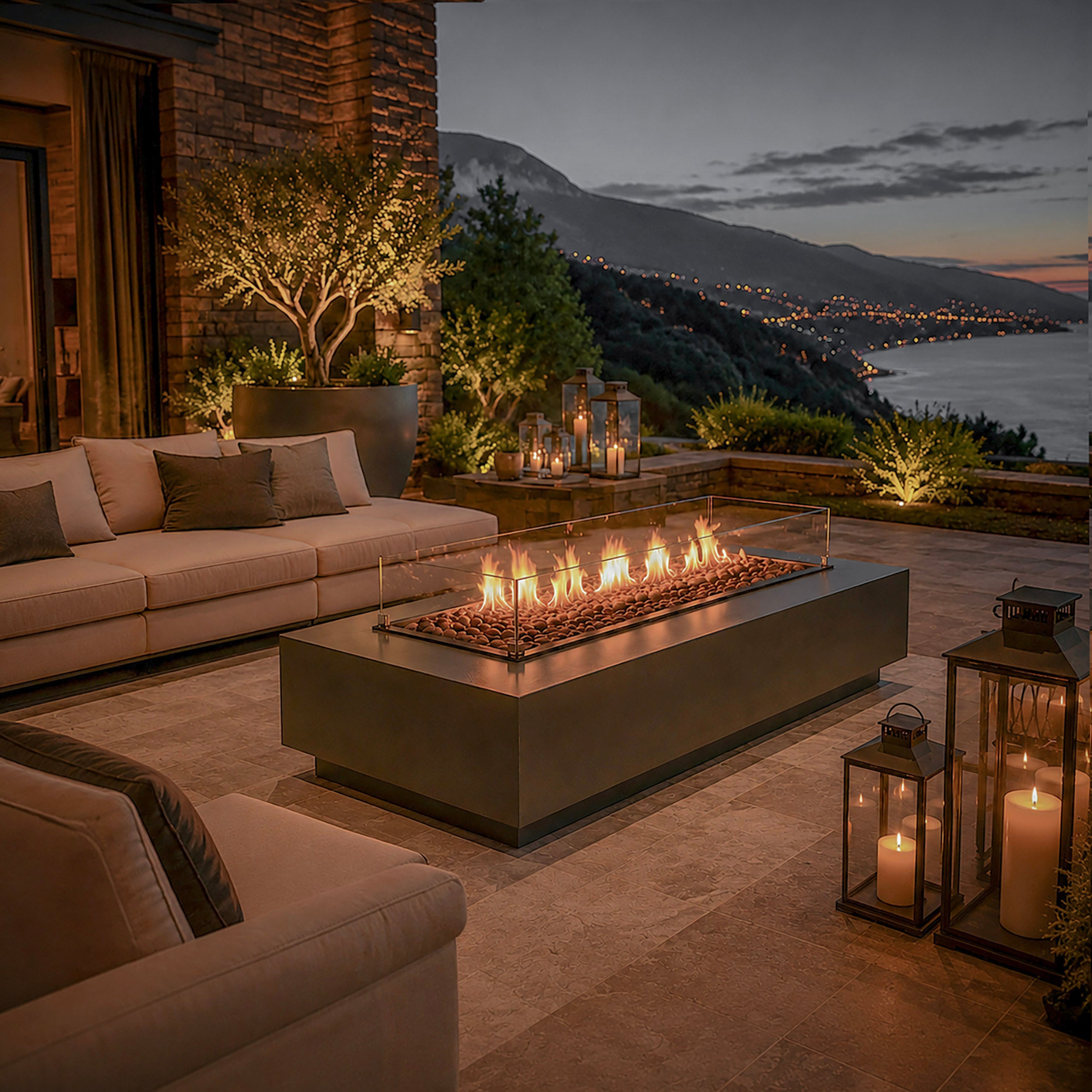 Aurora Flame luxe vuurtafel op een stijlvol terras met loungeset, sfeerverlichting en panoramisch uitzicht over de kustlijn tijdens de avond.